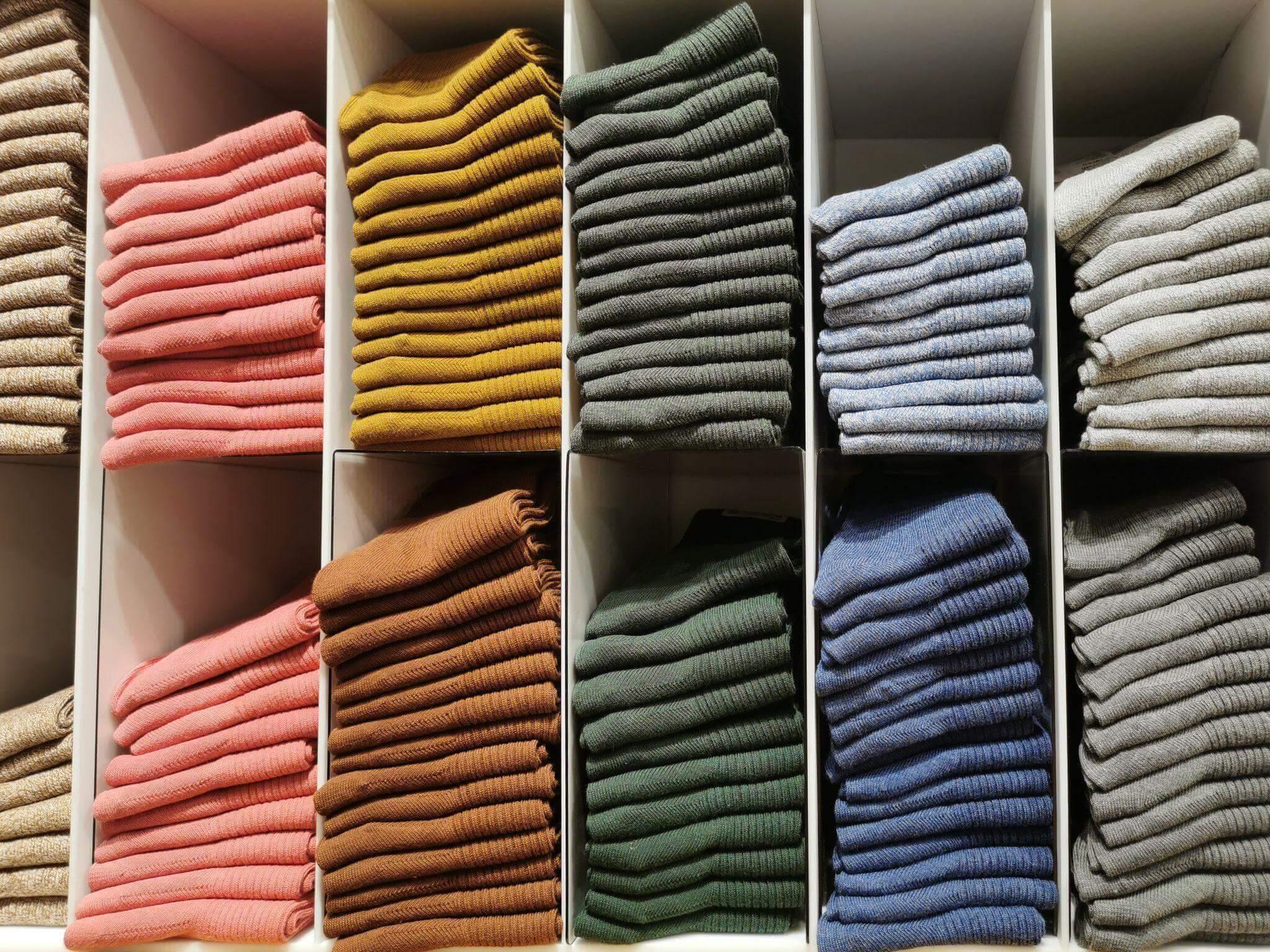 Scaffali pieni di maglioni piegati per colore - gestione dello stock e organizzazione delle taglie in una boutique di moda (approvvigionamento / grossista).
