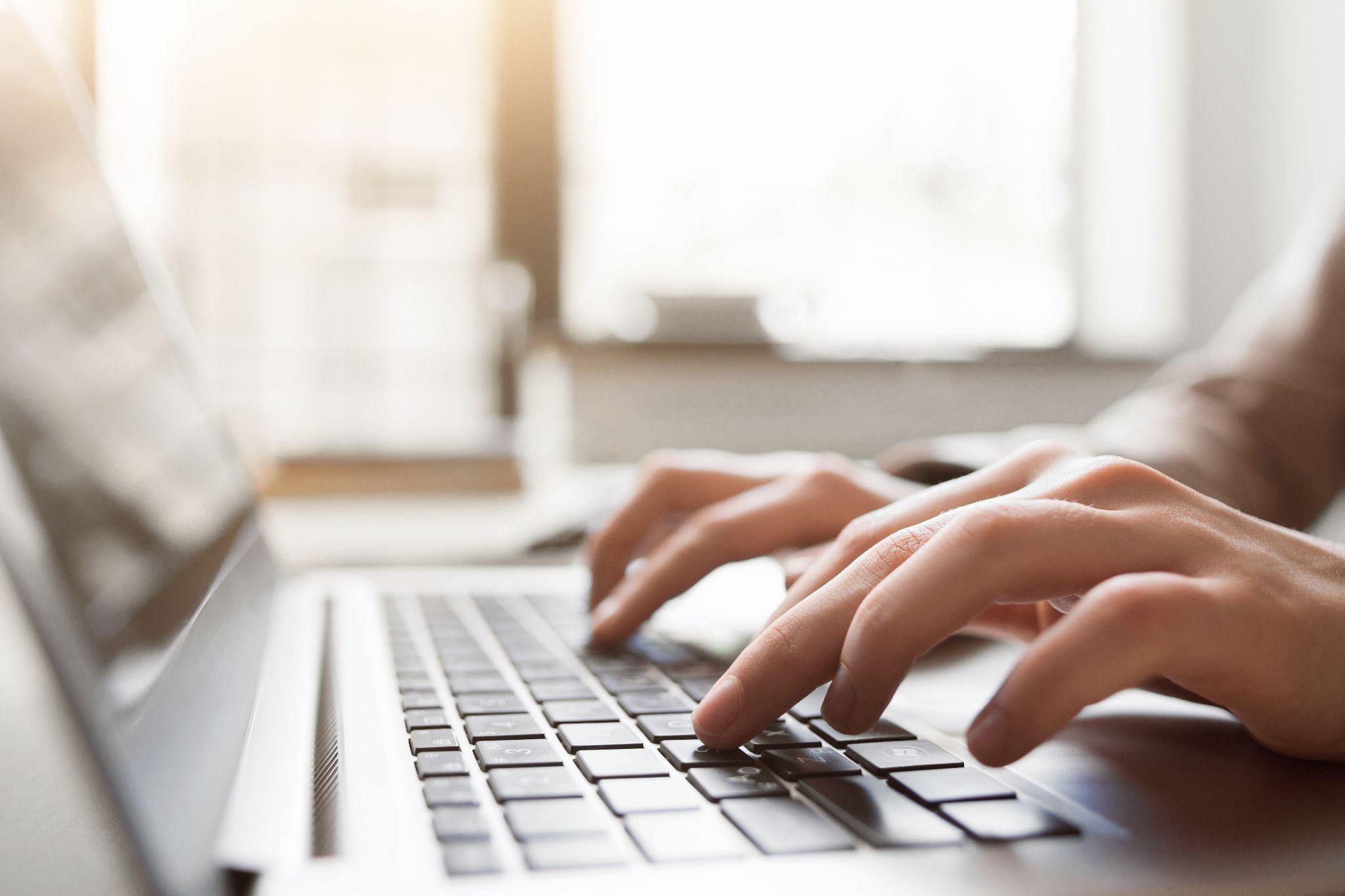 Deux mains tapent sur le clavier d'un ordinateur.