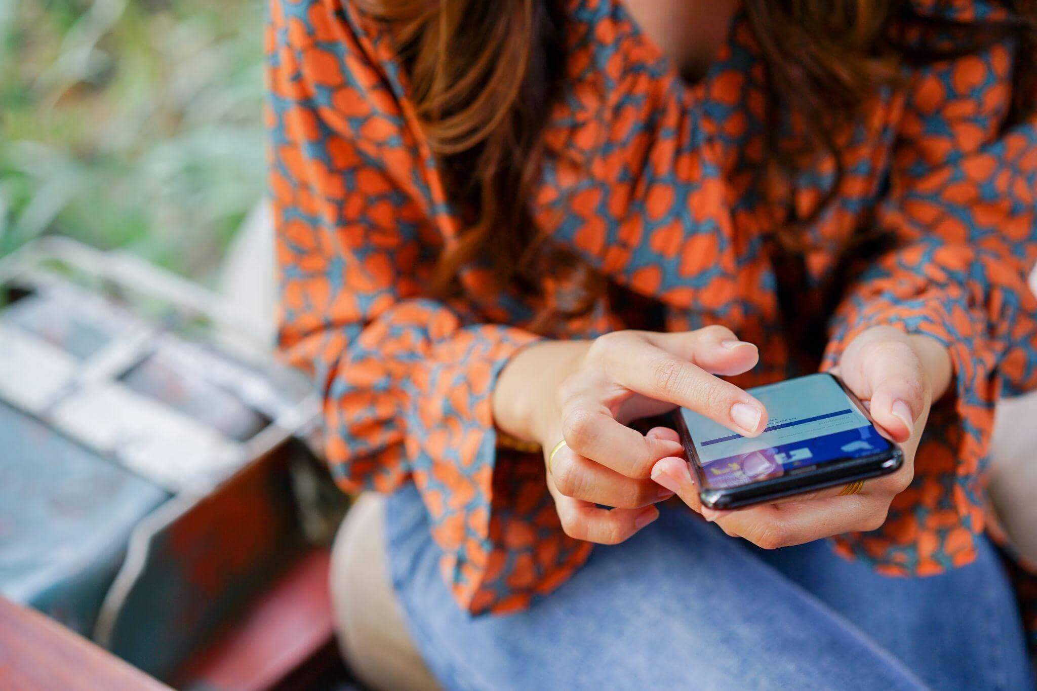 Femme assise en extérieur utilise son smartphone pour structurer une démarche de networking.