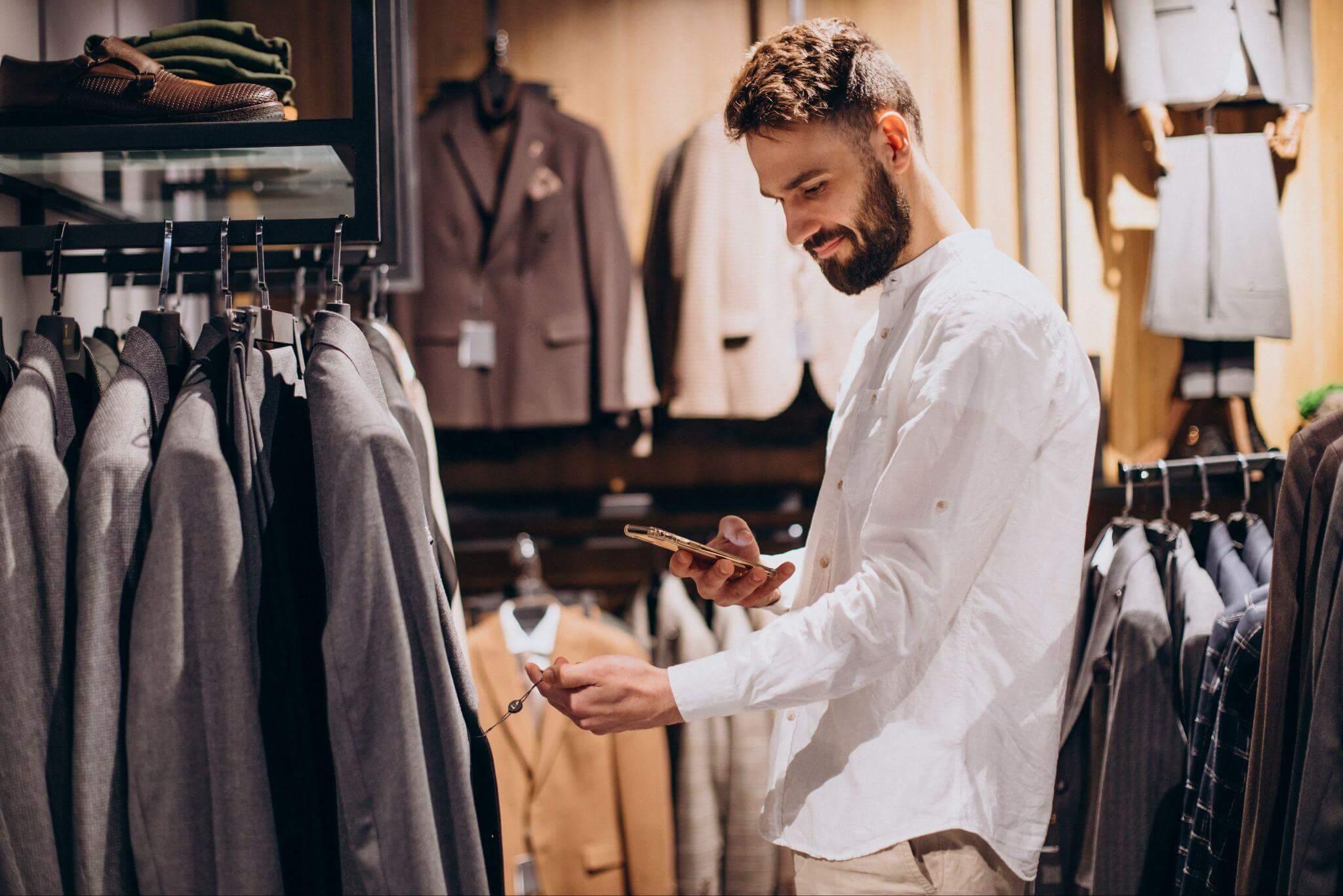 Un uomo sorridente in un negozio di abbigliamento. Guarda l'etichetta di una giacca e scatta una foto.