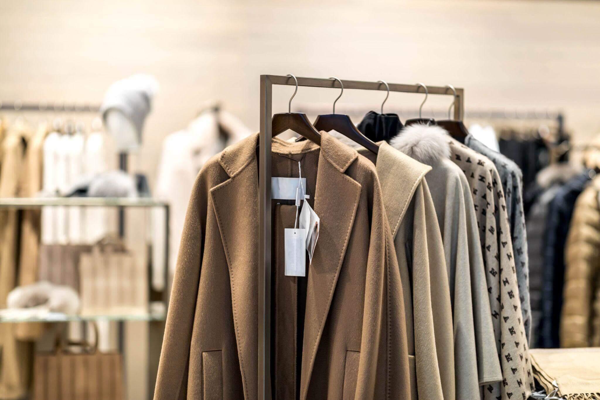 Scaffale di cappotti beige con cartellini dei prezzi in una boutique - assortimento di prodotti e merchandising nel prêt-à-porter (rifornimento all'ingrosso).
