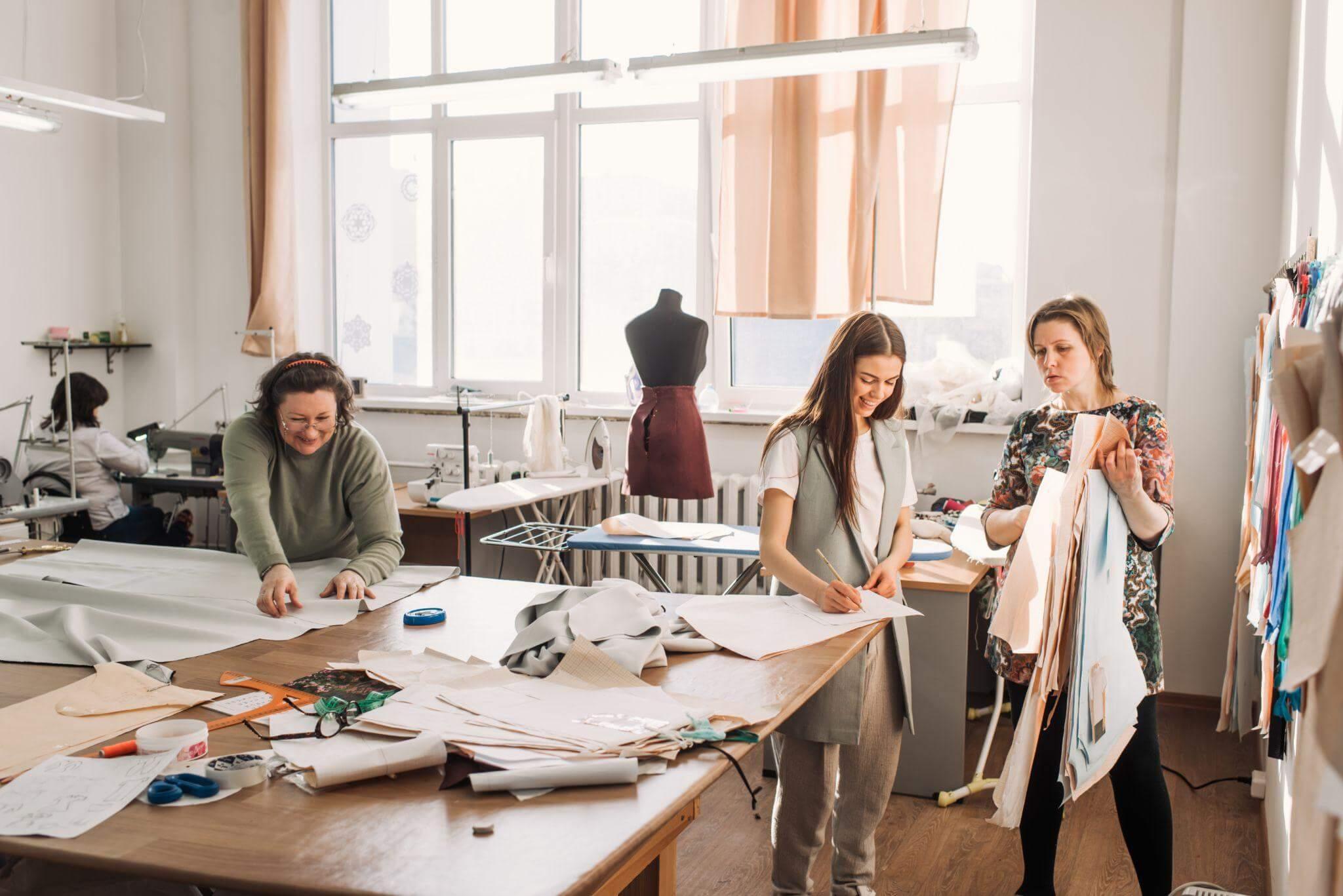 Tre donne sorridenti lavorano ai tessuti per la loro collezione in un laboratorio.