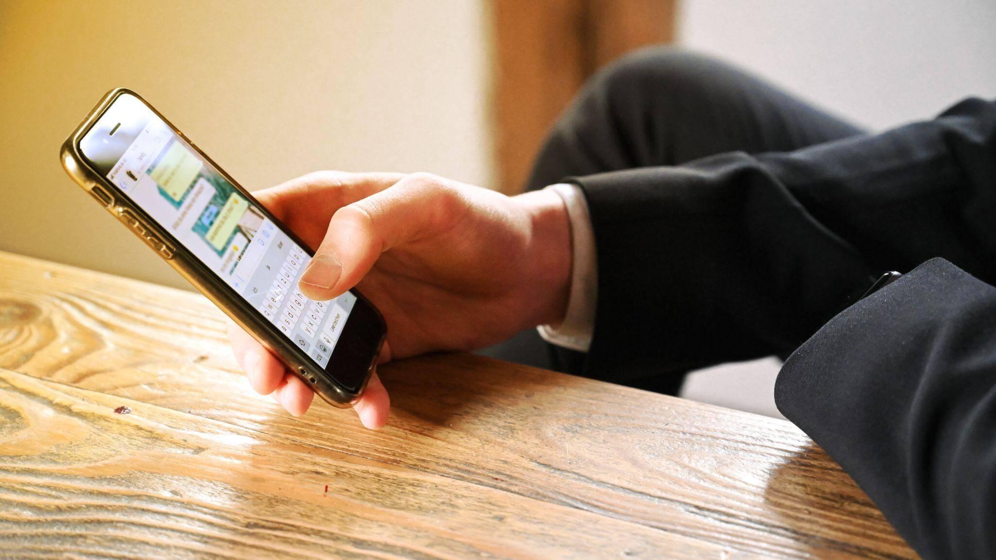 Un homme assis et accoudé à table utilise son smartphone pour vendre en ligne avec WhatsApp.