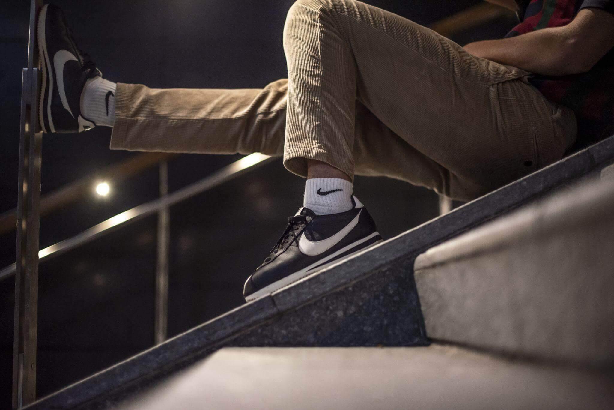 Un uomo è seduto sui gradini di una scala esterna. Indossa scarpe da ginnastica bianche e nere di un marchio di abbigliamento e sport con calzini abbinati.