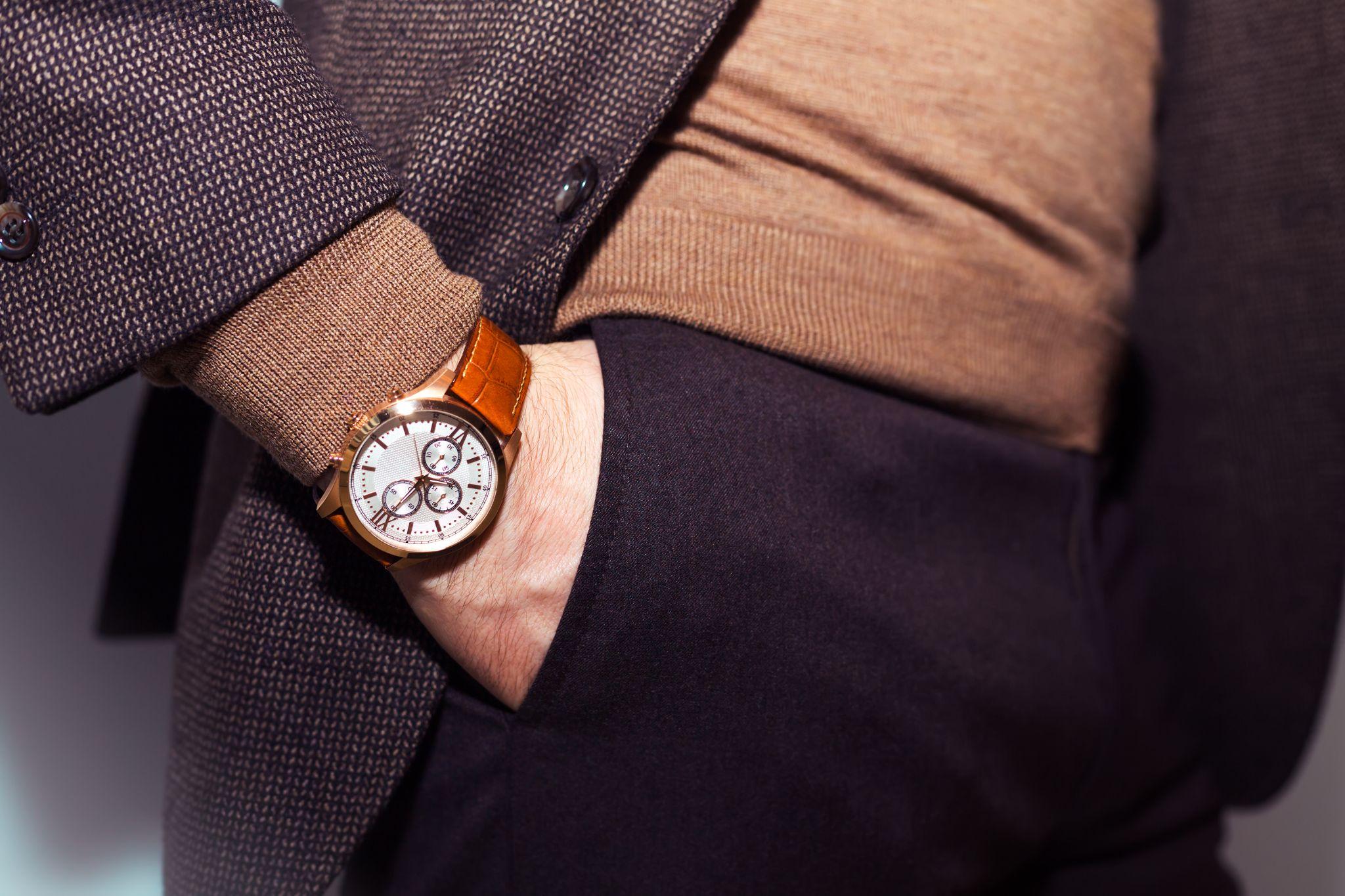 Un homme à la main dans la poche. On voit très clairement une montre de qualité et des vêtements chics.
