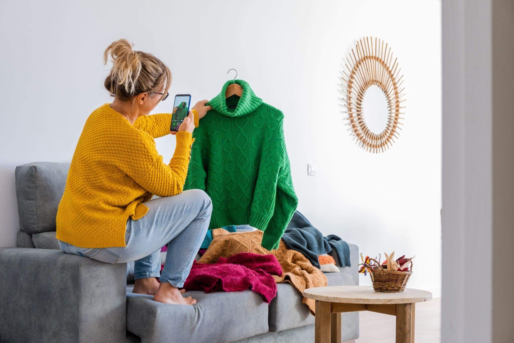 Una donna seduta sul suo divano fotografa i suoi vestiti per metterli in vendita su Vinted.