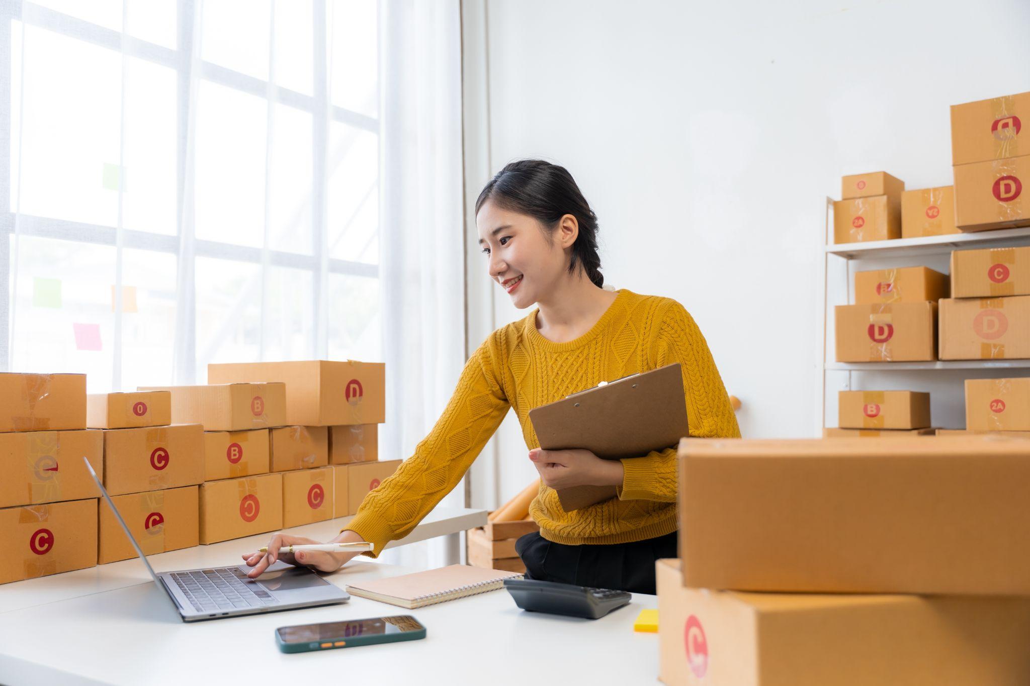 Une femme entourée de cartons utilise son ordinateur pour sélectionner de bons fournisseurs et partenaires de confiance. 