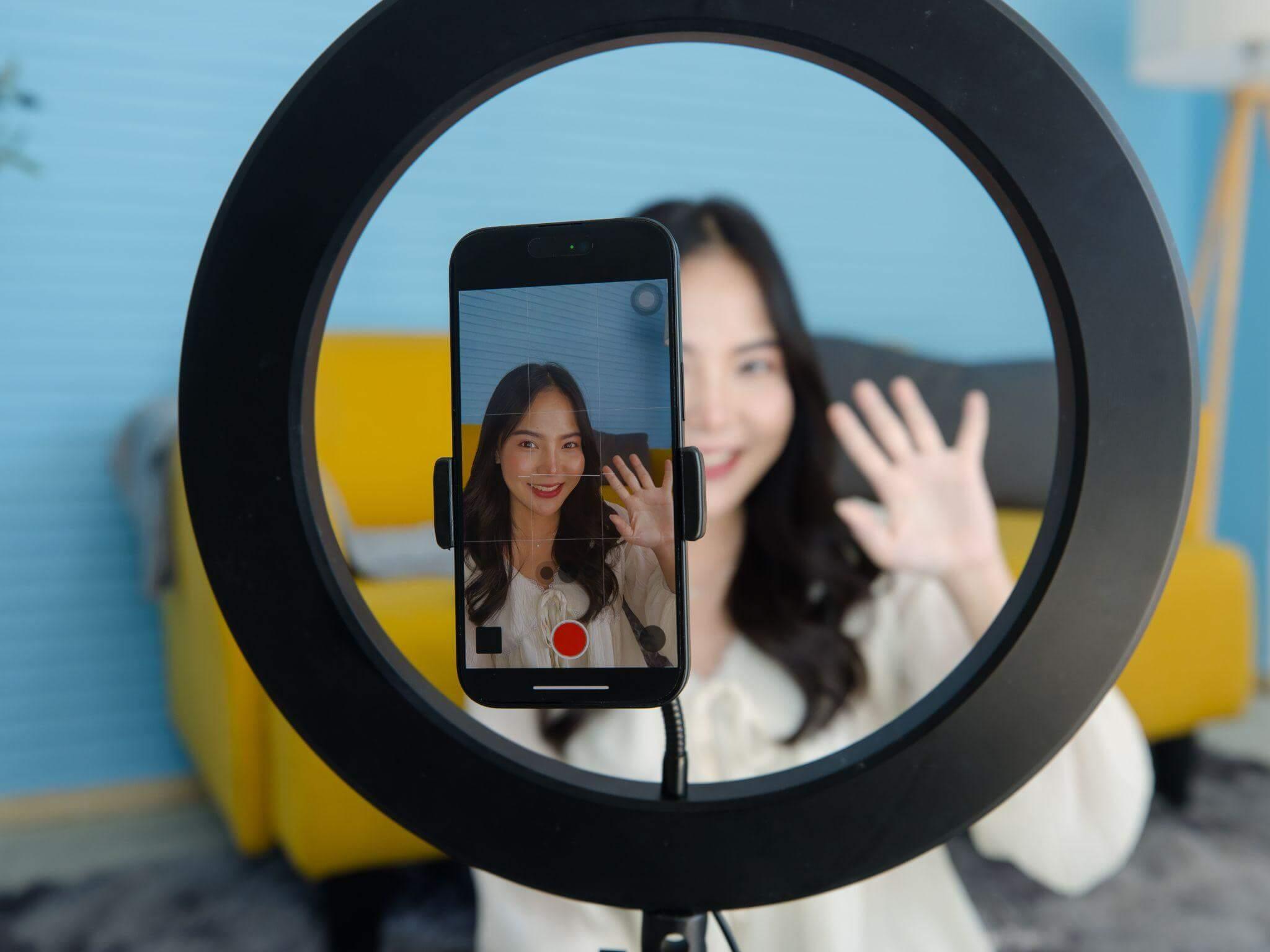 Une femme se filme avec son smartphone, elle est équipée d'une ring light et travaille sur une communication transparente.