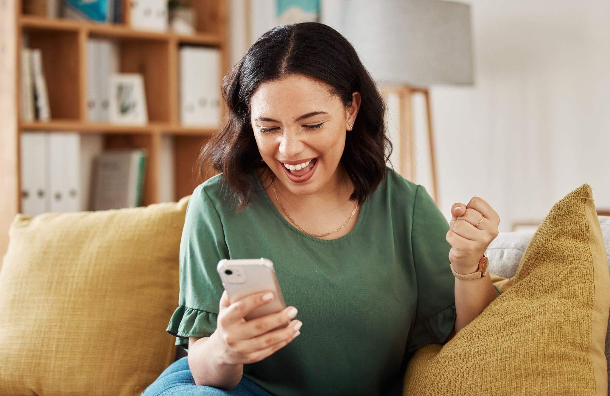 Une jeune femme assise, se réjouit devant son smartphone.