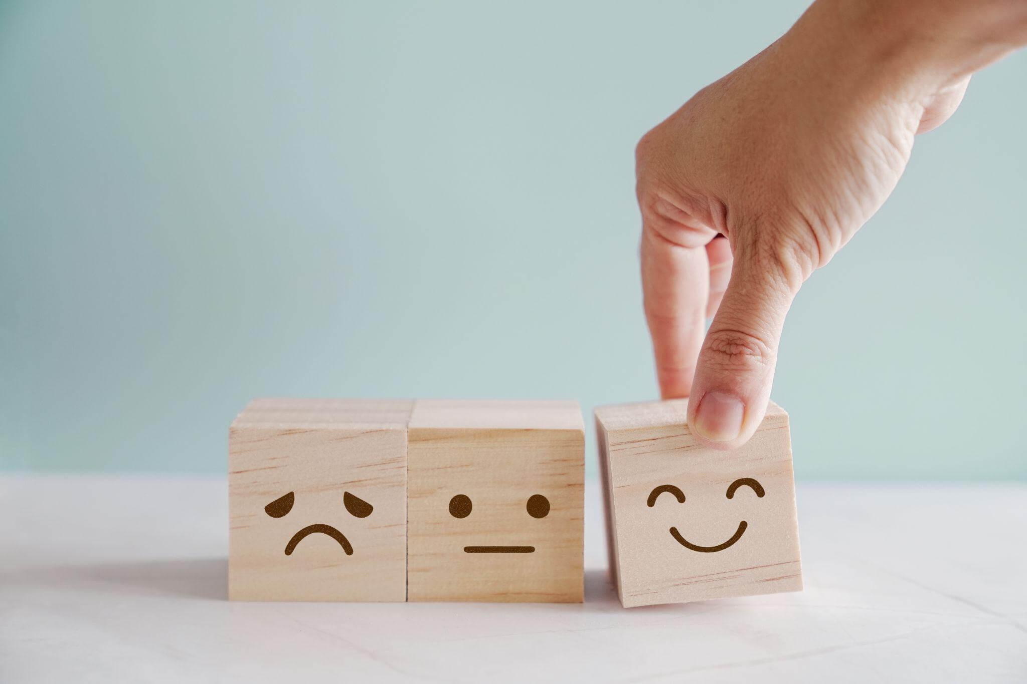 Une main replace des cubes de bois présentant des visages qui vont du négatif au positif. La main replace le cube positif.